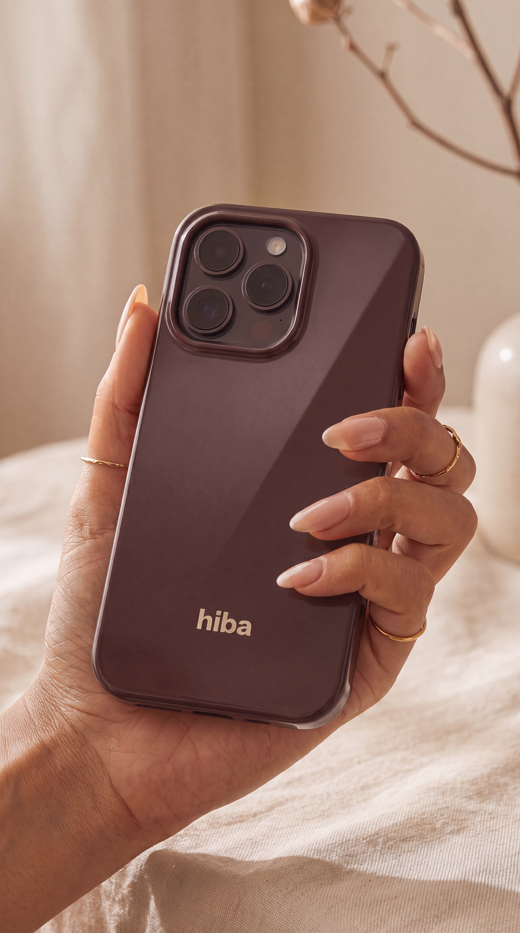 A feminine hand cradles the glossy Cocoa HIBA case in warm daylight