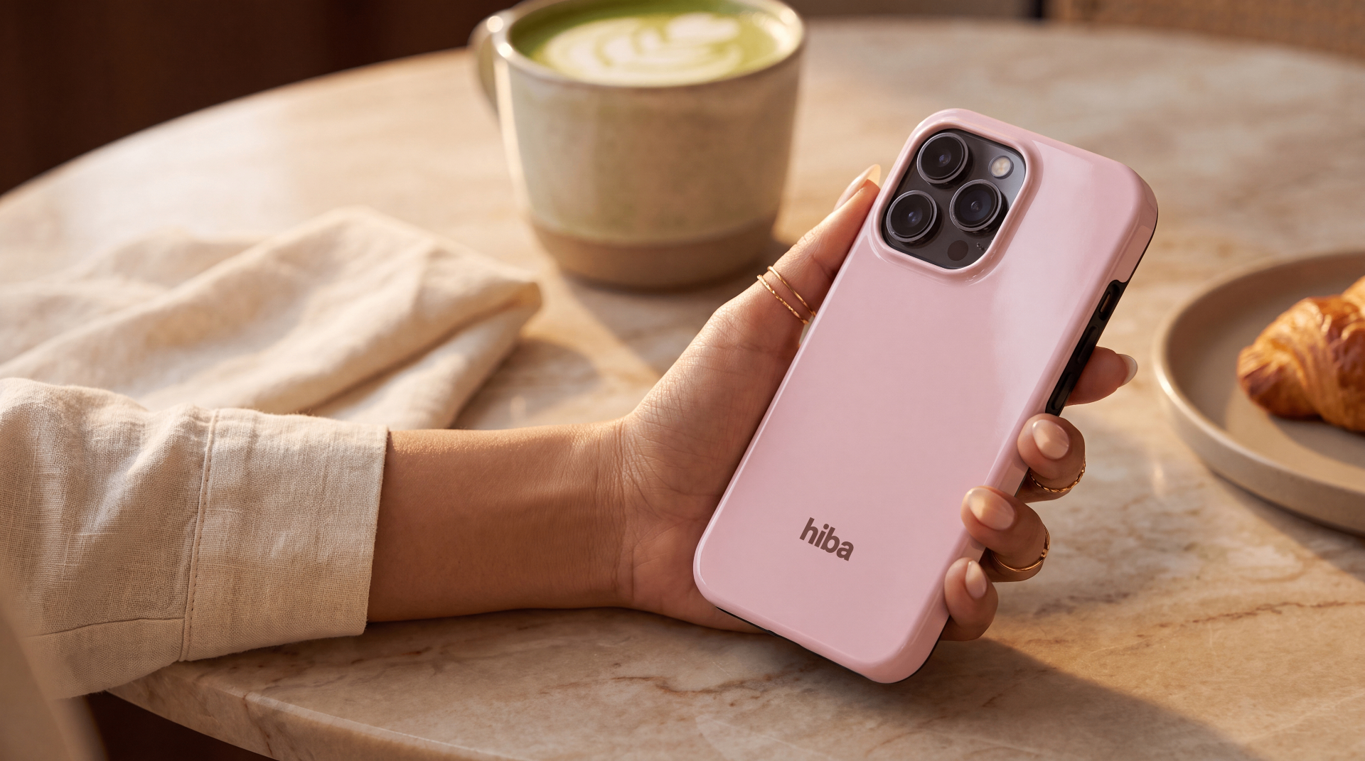 a blush hiba case held over a warm café table with matcha and croissant