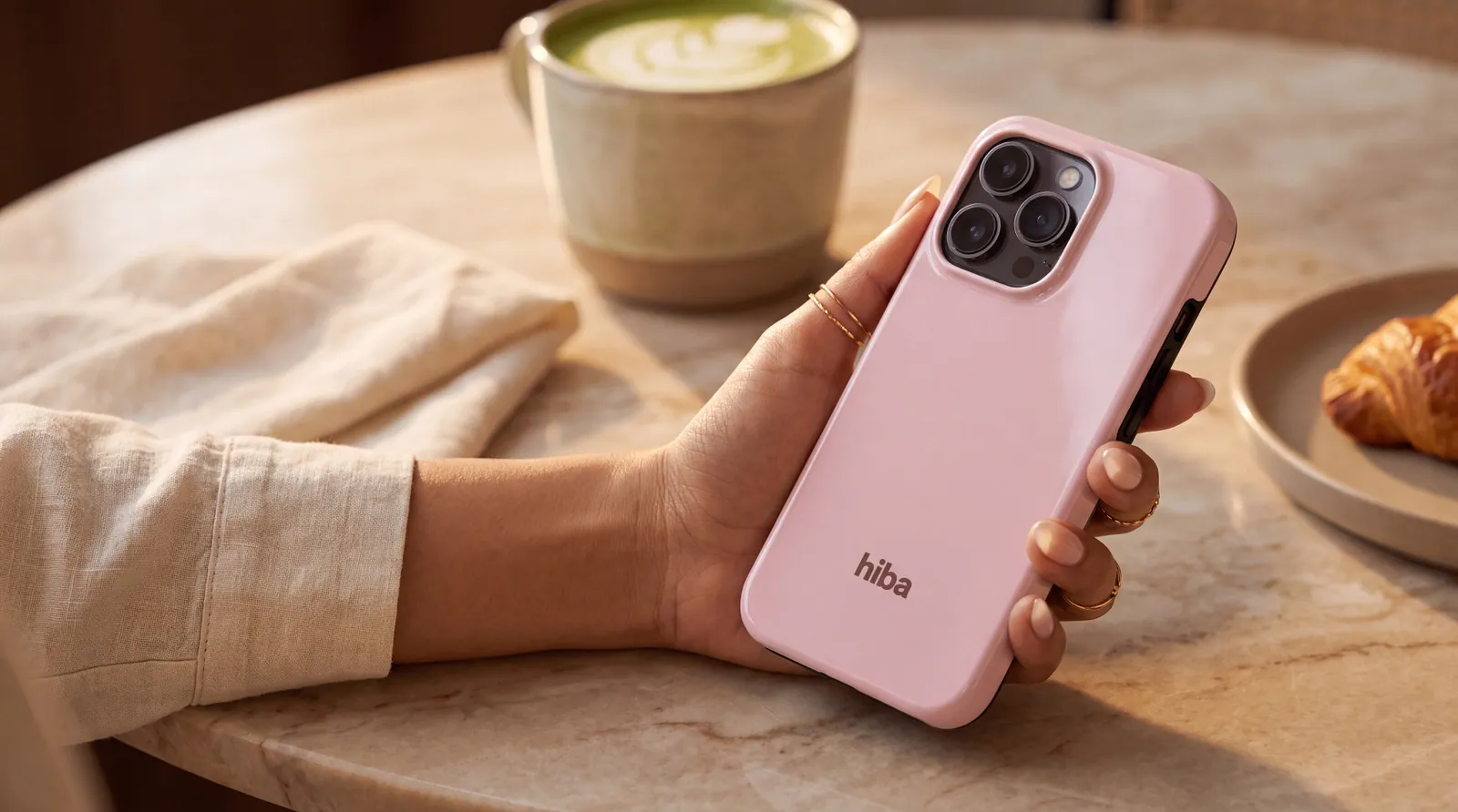 a blush hiba case held over a warm café table with matcha and croissant